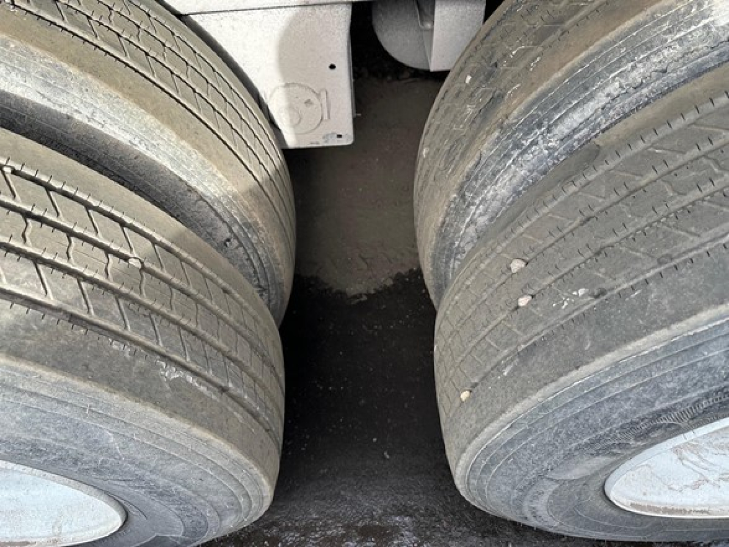 Flatbed trailer axle area with dual tires and mud residue showing tread details and wheel hubs.
