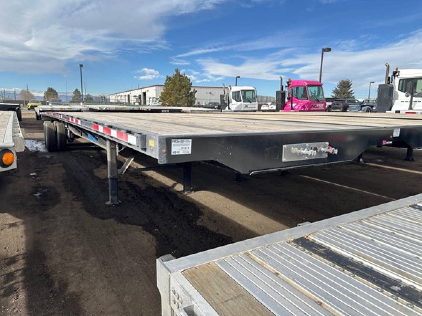 Flatbed trailer showing low deck with steel frame and support legs, side markers, and label plates on the front left side.