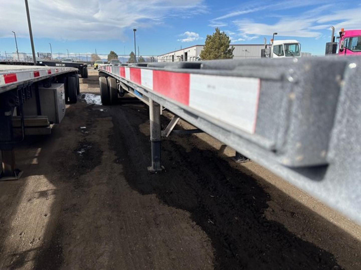 Trailer side view of a used 2024 Wabash air ride steel flatbed showing red and white reflective beadboard along the top edge.