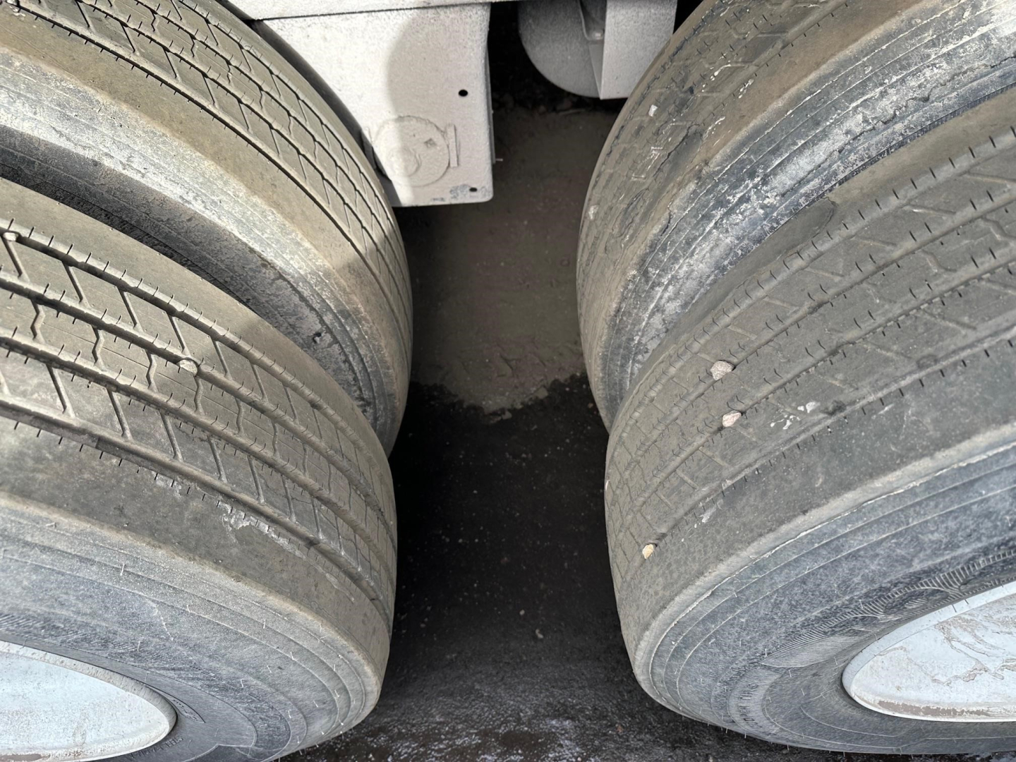 Flatbed trailer dual rear wheels showing tread and spacing, with axle area and part of frame visible.
