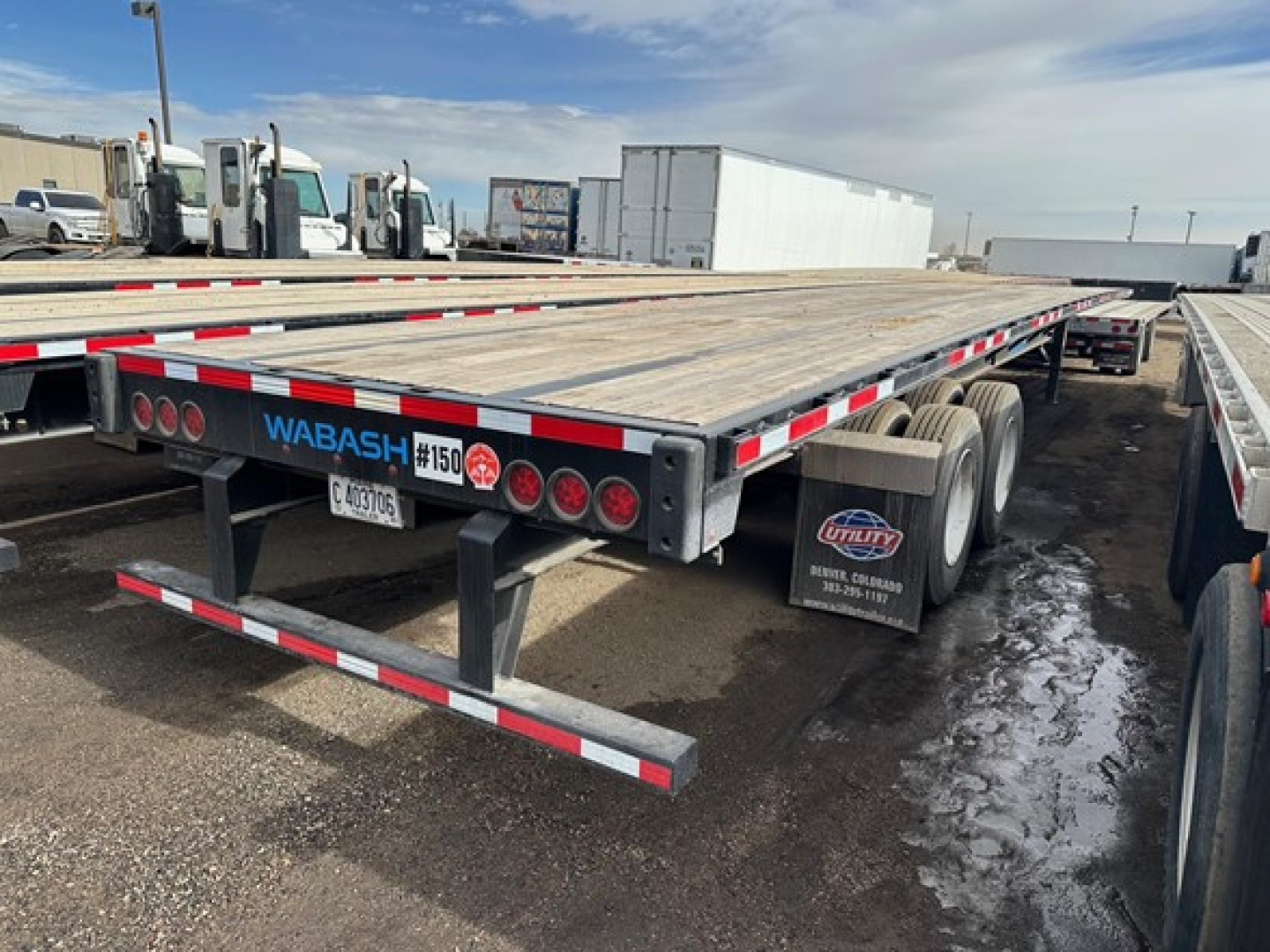 Flatbed trailer rear showing Wabash logo, 150 sticker, taillights, and reflective safety markings; wooden deck; mud flaps; dual rear axles.