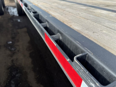 Flatbed trailer side viewed edge showing wooden deck and steel frame with reflective red stripe.