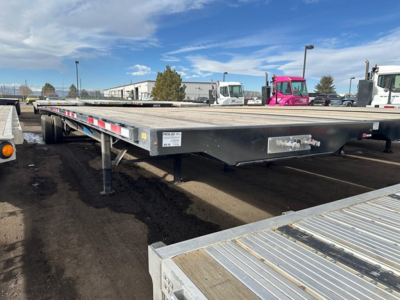 Flatbed trailer showing low deck with steel frame and support legs, side markers, and label plates on the front left side.