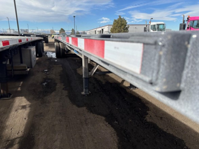 Flatbed trailer side showing steel frame with red-and-white reflective markings under clear sky.
