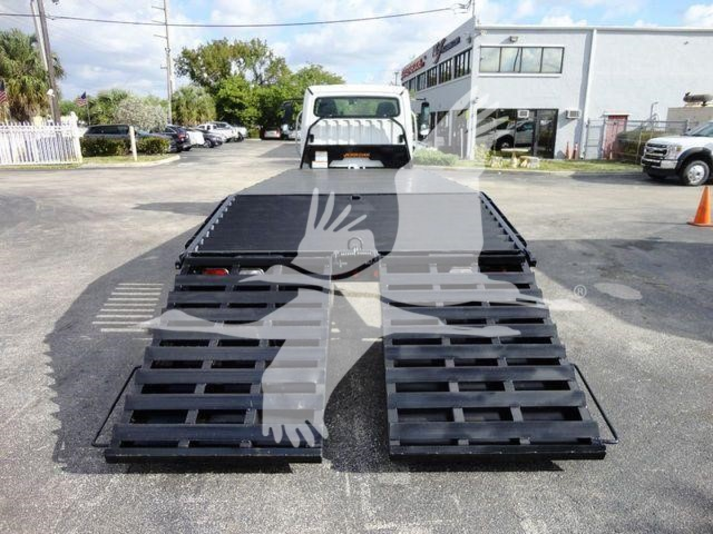 Flatbed tow truck with two black ramps extended, rear view shows bed and small cab; watermark obscures center.