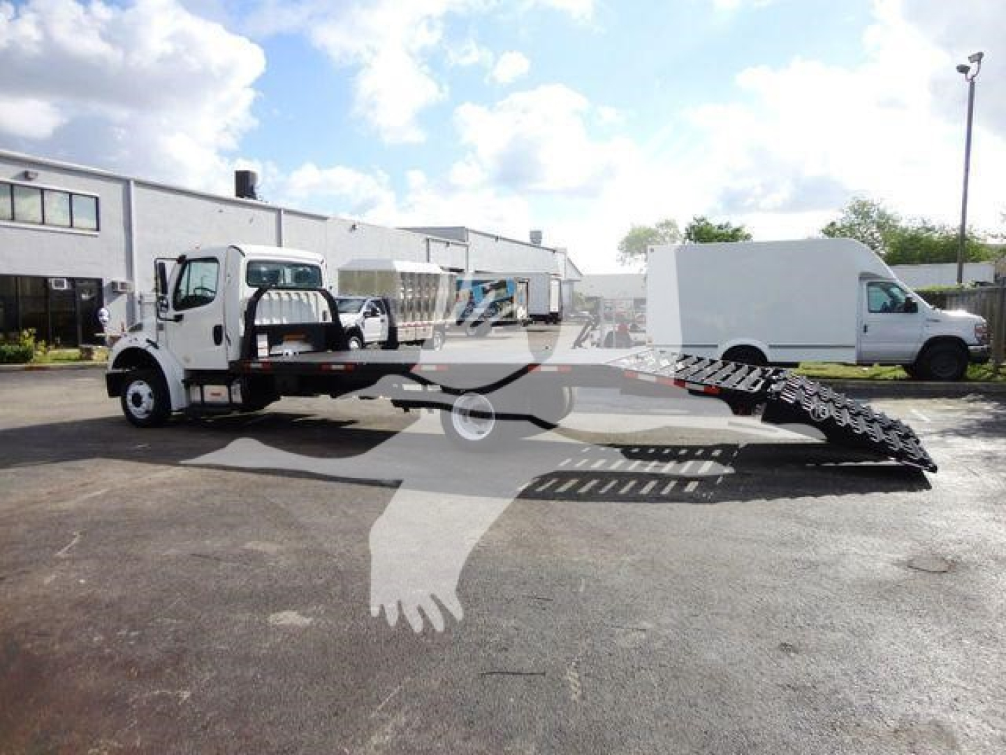 Flatbed tow truck with a hydraulic ramp and a white cab, Freightliner M2 106, side view showing flatbed area and ramp extended.