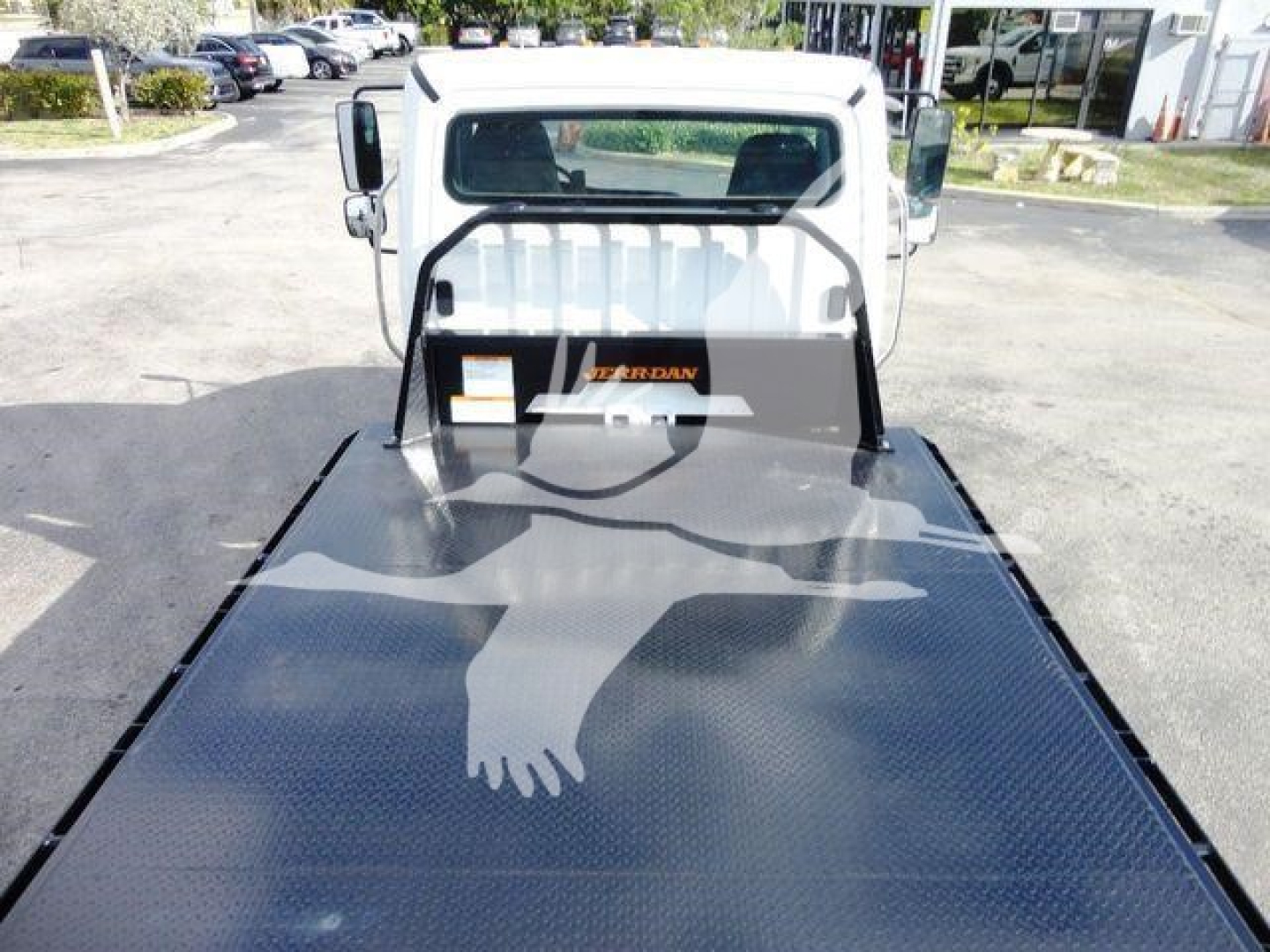 Flatbed truck bed of a 2015 Freightliner M2 106 with a diamond plate surface and a white cab, front view showing windshield and headache rack.