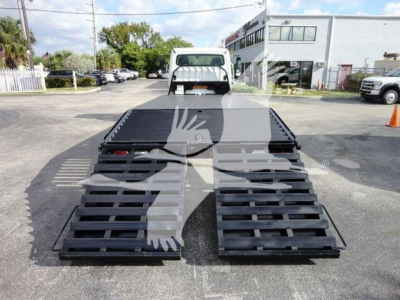 Flatbed tow truck with two black ramps extended, rear view shows bed and small cab; watermark obscures center.