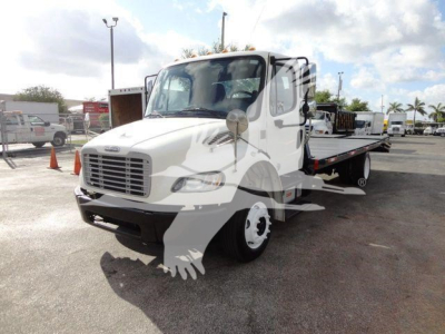 Flatbed tow truck in a dealership lot showing Freightliner M2 106 cab and flatbed with VIN plate visible.