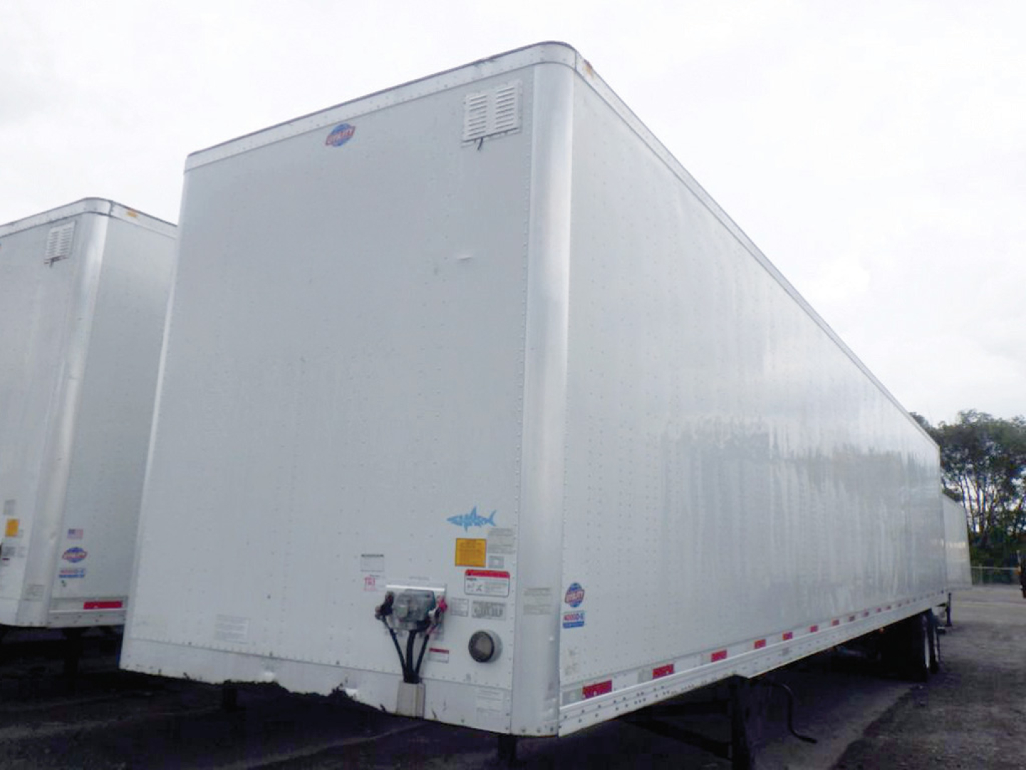 Utility dry van trailer side/front view showing exterior white panels, rear door hardware and reflective tape along base line.