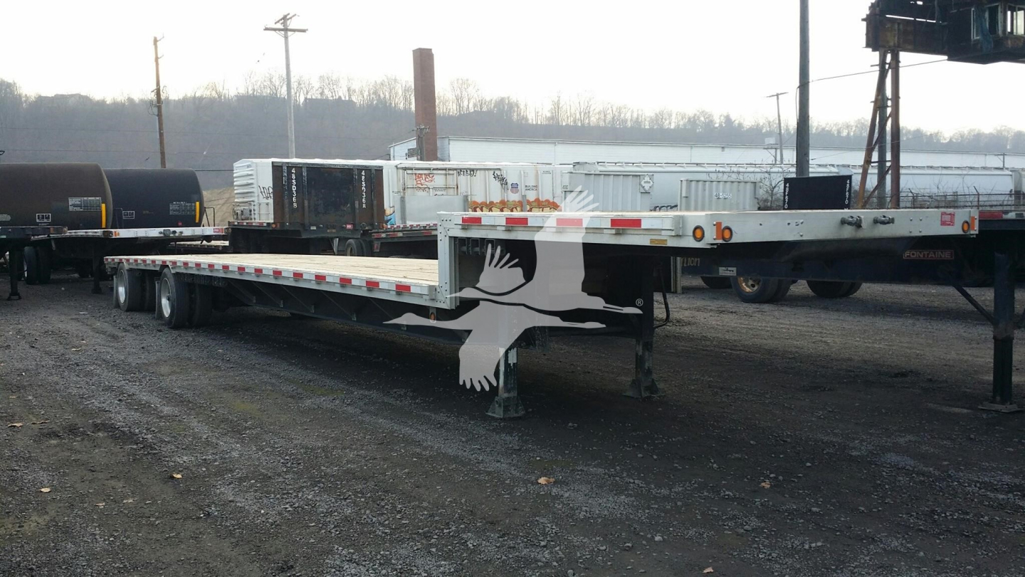Deck trailer showing wooden bird decal on front, long drop deck with dual rear axles, hitch and support structure visible.