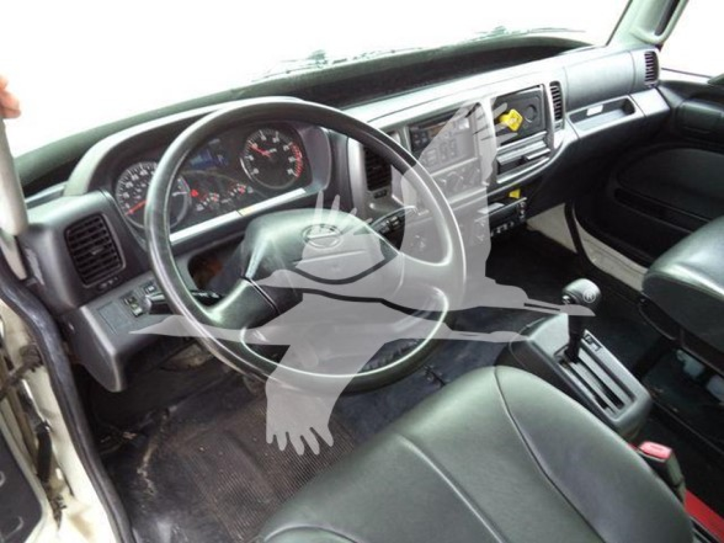 Truck cab interior showing steering wheel, dashboard, gear selector, and front seating. Visible controls and gauges in the dashboard area.