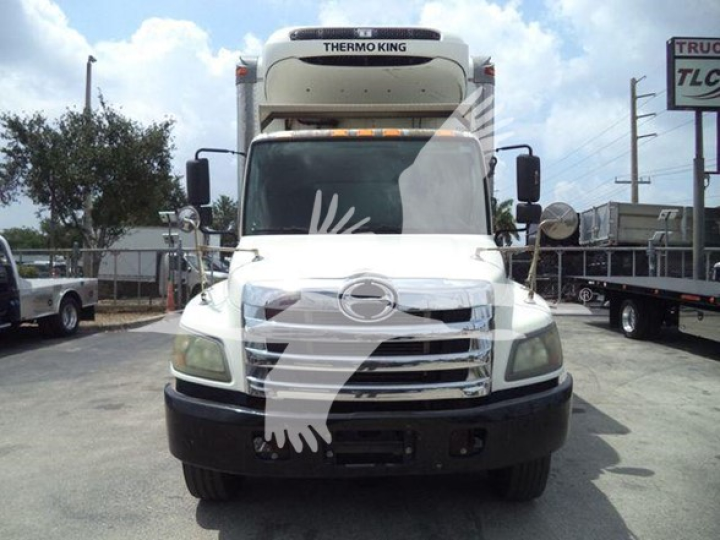 Hino 268A refrigerated truck front view with Thermo King unit on cab, white cab, black bumper, two mirrors, and cargo area in background.