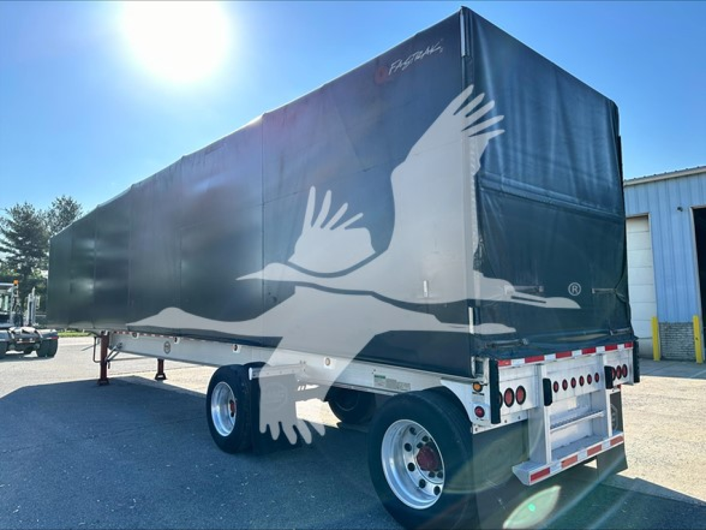 Curtainside trailer showing graphic of a white bird in flight on a dark green surface with rear lights and bumper.