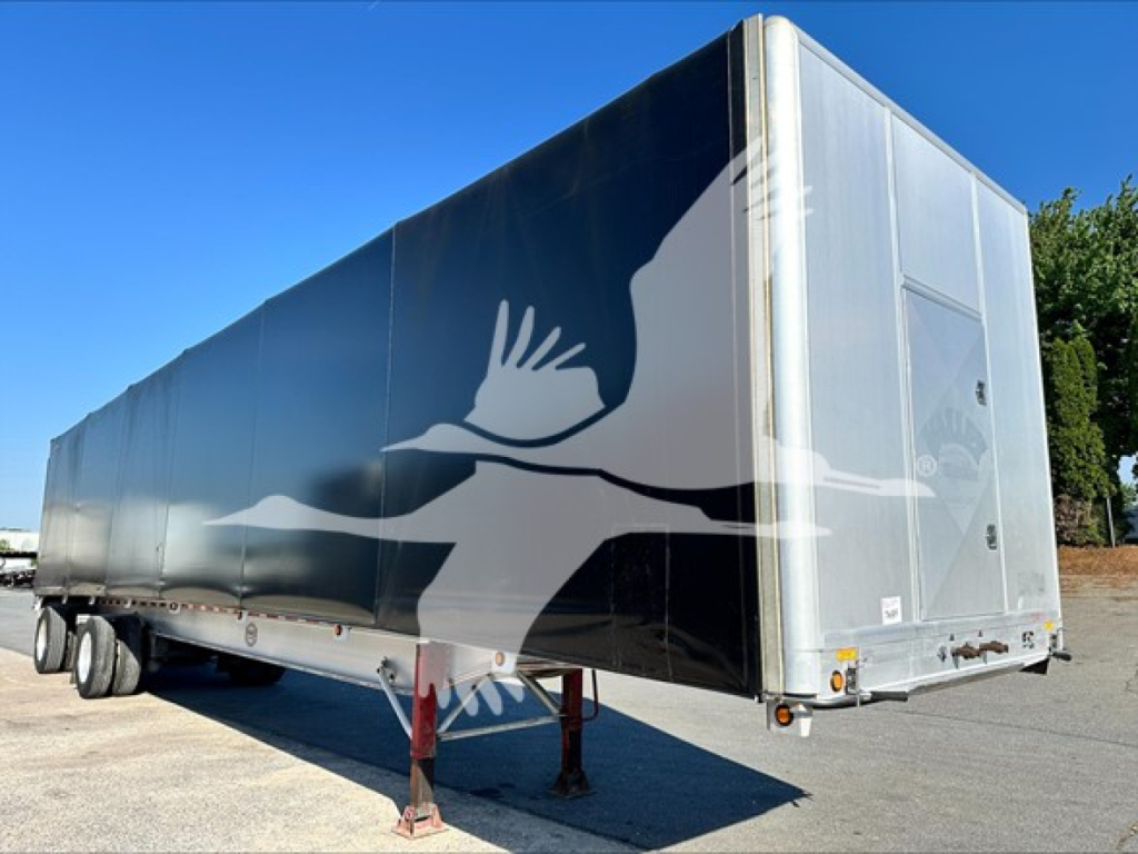 Curtainside trailer with black and gray paint, large side graphic of a bird in flight on the side, silver front/ rear corner posts, landing gear visible, tires at rear.