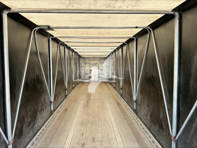 Inside view of a curtainside trailer in a warehouse, showing a long metal interior with vertical support bars and a ribbed floor.