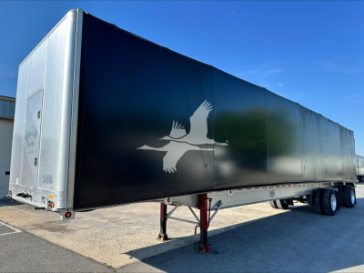 Trailer side with a graphic of birds in flight, black exterior, white logo near center, and rear lighting and support legs visible.