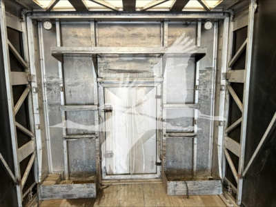 Curtainside trailer interior with metal framing, door in center, shelves and brackets along walls, weathered aluminum surfaces.