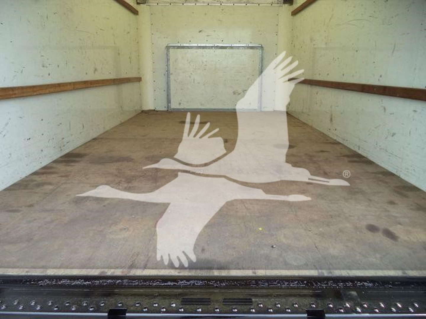 Ford E-350 XL SD cargo box interior showing empty plywood floor and sidewalls, with rear ramp door and circular logo watermark.