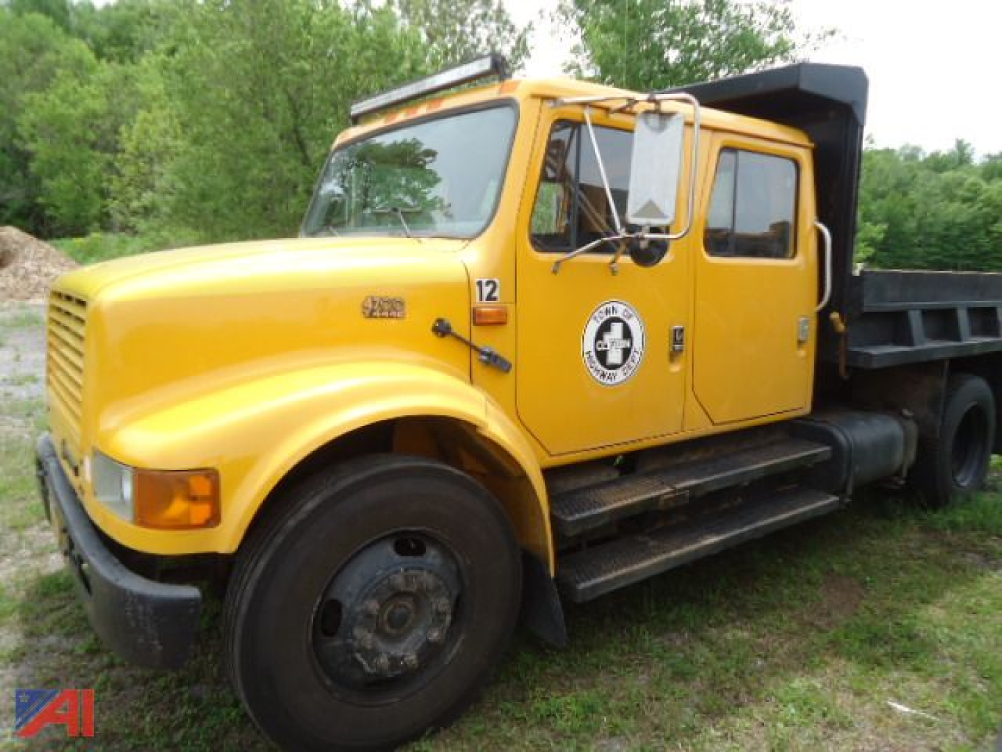 1997 International 4700 dump truck in yellow, side view showing dump bed, front wheel, and side step.