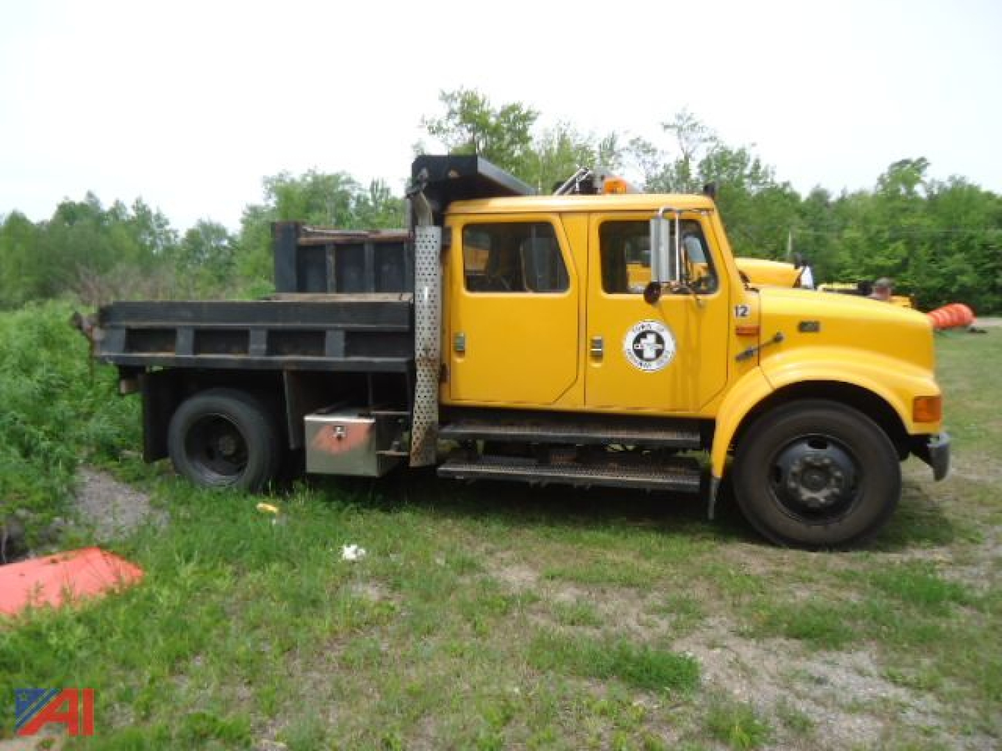 International 4700 dump truck in service view showing yellow cab and black dump bed with side toolbox.