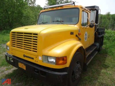 International 4700 dump truck in yellow with black bumper and side steps, front grille, emblem on door, and orange beacon light on cab roof.