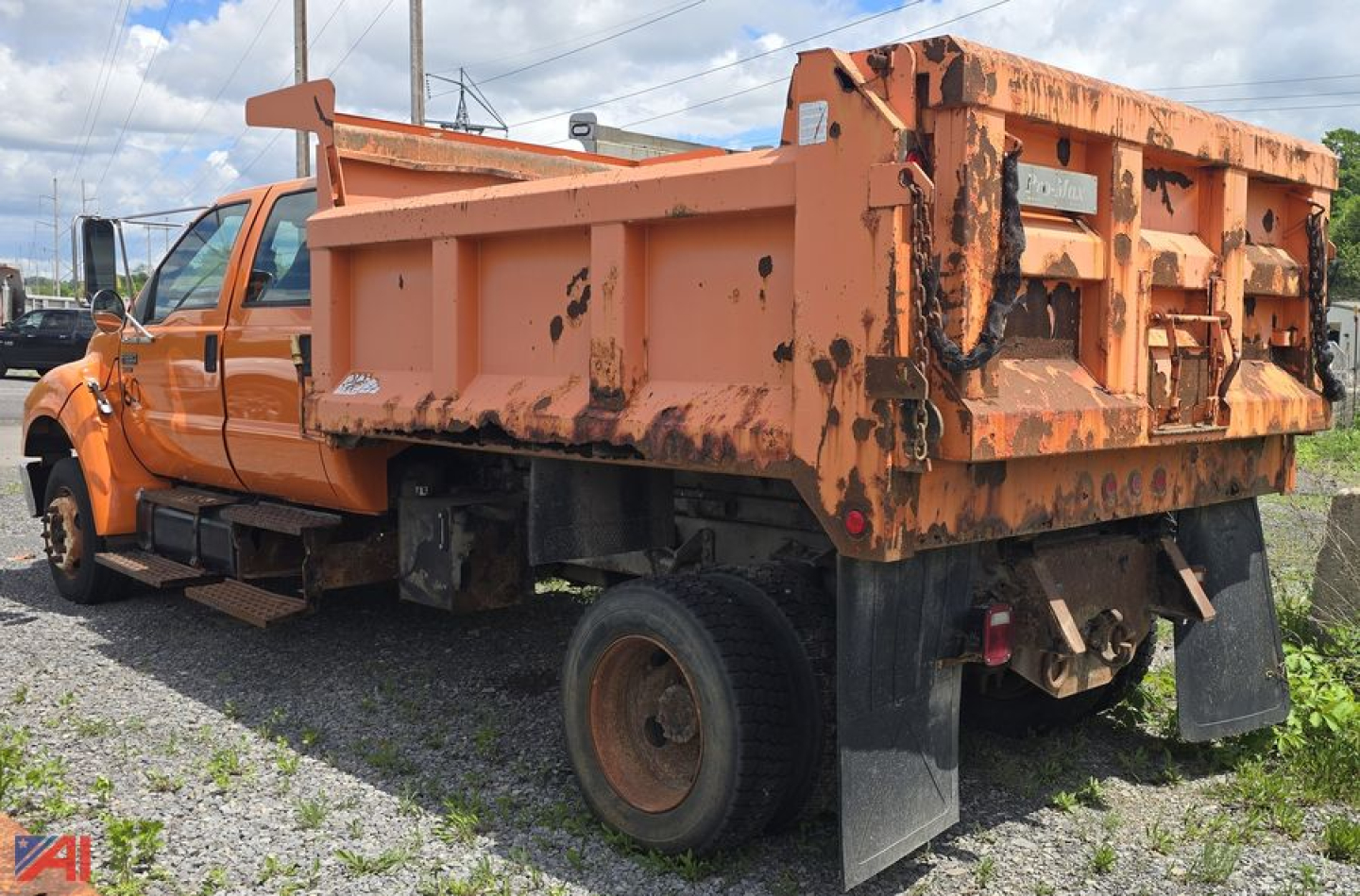 Footage of an orange Ford F-650 dump bed truck with wear on the bed sides, showing the rear and left side. The dump bed has rust-like stains, and a black mudflap is visible behind the rear wheels.