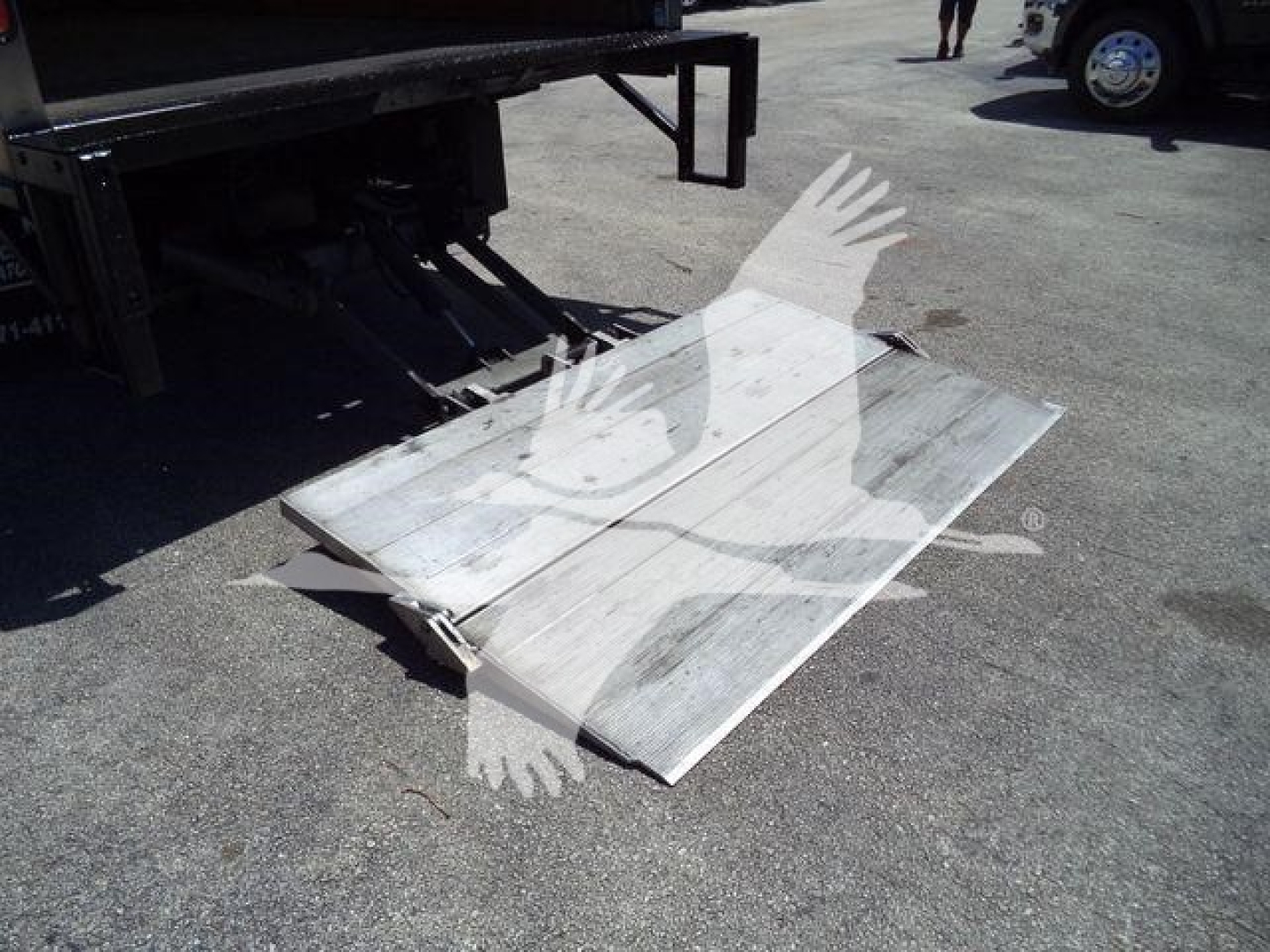 Isuzu NPR-HD truck ramp/platform lowered from rear with metal fold-out ramp on asphalt.