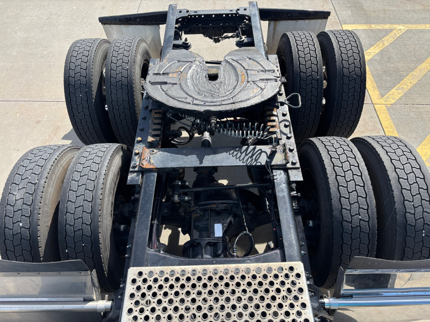 View of Kenworth T680 chassis rear showing fifth wheel, dual rear axles, and multiple tires; mechanical frame and components visible underneath.