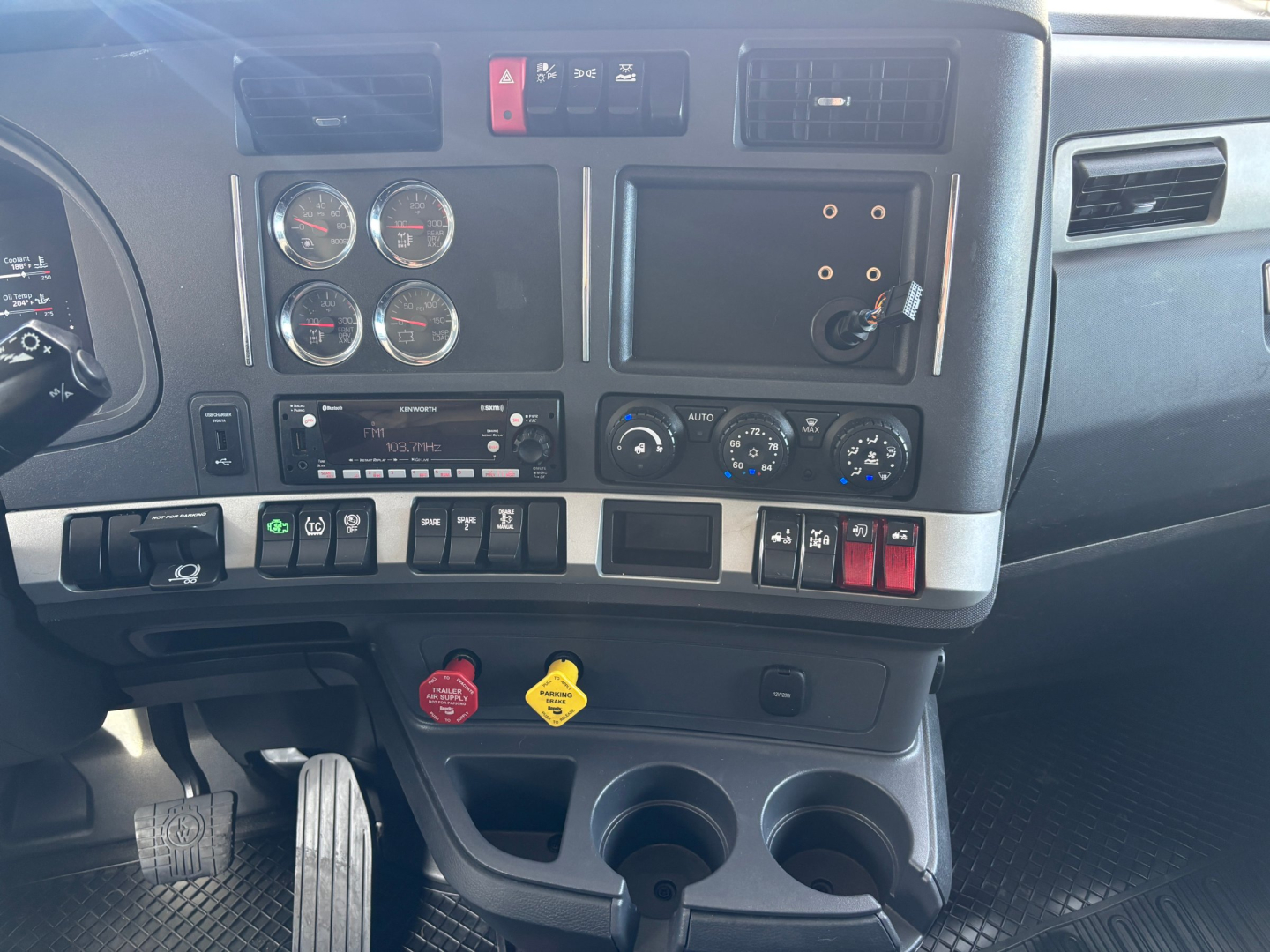 Kenworth T680 dashboard and center console showing gauges, switches, and cup holders.