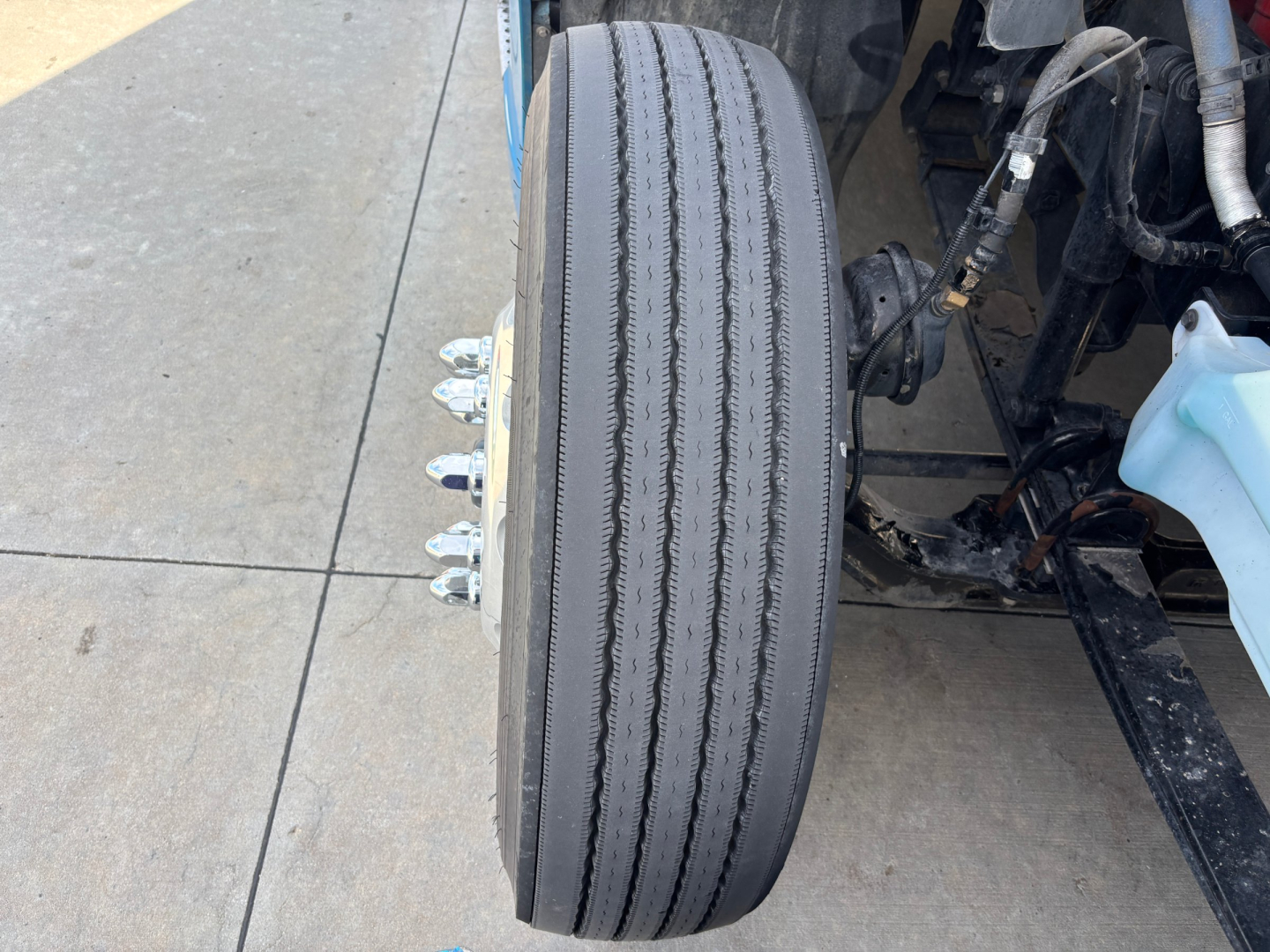 Kenworth truck front wheel and suspension components, with multiple lug nuts and tire tread visible.
