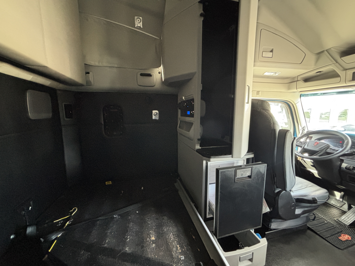 Kenworth T680 interior cab area showing sleeper cabinet, storage drawer, and cockpit with steering wheel and dashboard.