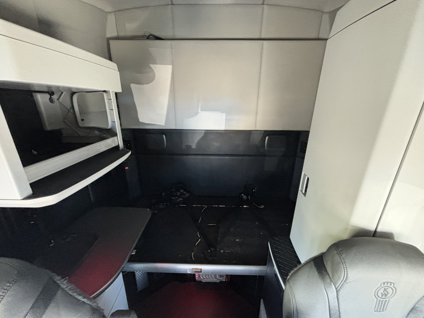 Cab interior of a Kenworth T680 sleeper showing overhead storage, partitions, and vertical cabinets with a dark floor and a raised step.