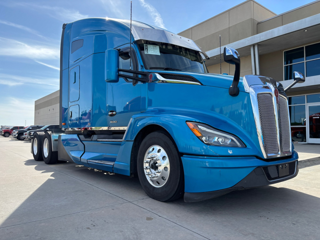 Kenworth T680 tractor-trailer in blue front-left view showing aerodynamic sleeper cab and chrome grille.