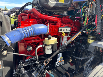 Kenworth T680 engine bay showing red engine labeled EX15 with blue intake hose, yellow oil reservoir cap, and various wiring harnesses.