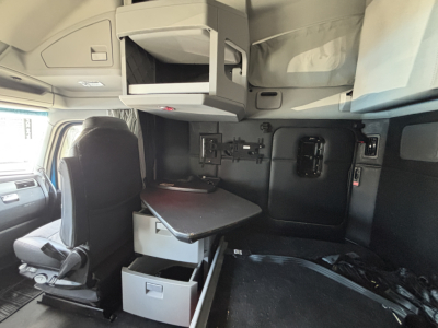 Kenworth T680 cabin interior showing seating and sleeper area with mounted monitor shelf and desk in view.