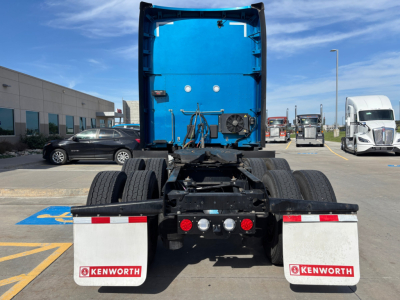 Rear view of a Kenworth truck chassis in a dealership lot with blue cab back panel and two white Kenworth mud flaps.