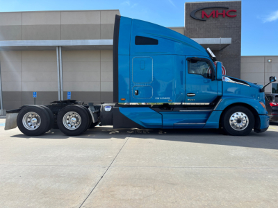 Blue Kenworth T680 sleeper tractor side view showing 6x4 rear axle configuration and MHC dealership building in background.