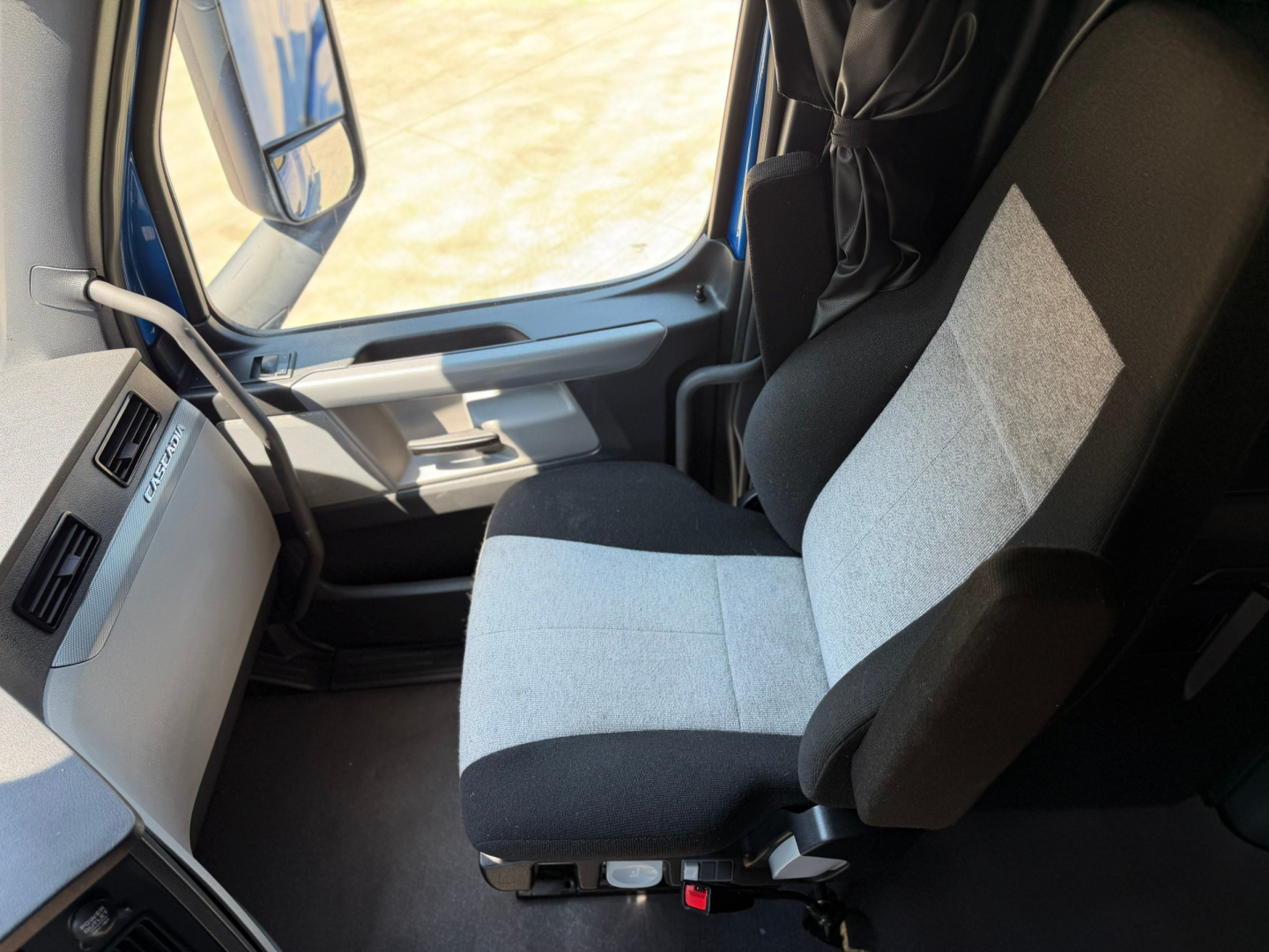 Cab interior of a Freightliner truck with two-tone gray and black seats, steering area, and dashboard.