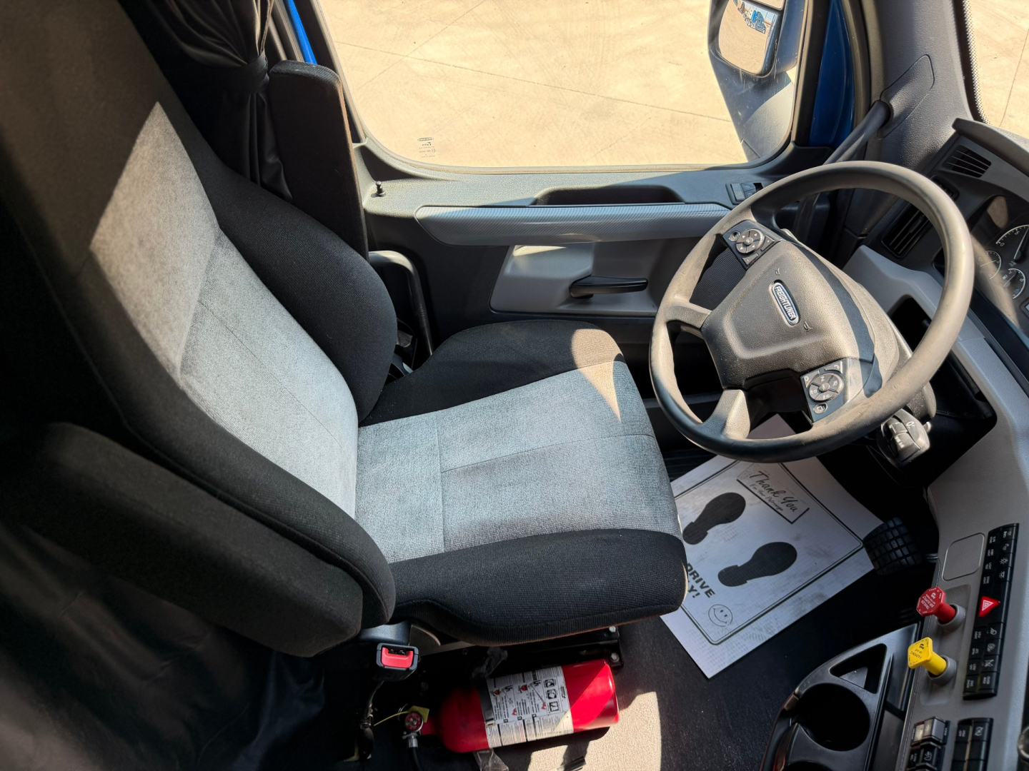 Truck cab interior of a Freightliner PT126064ST showing driver seat, steering wheel, dashboard, and gear controls in view.