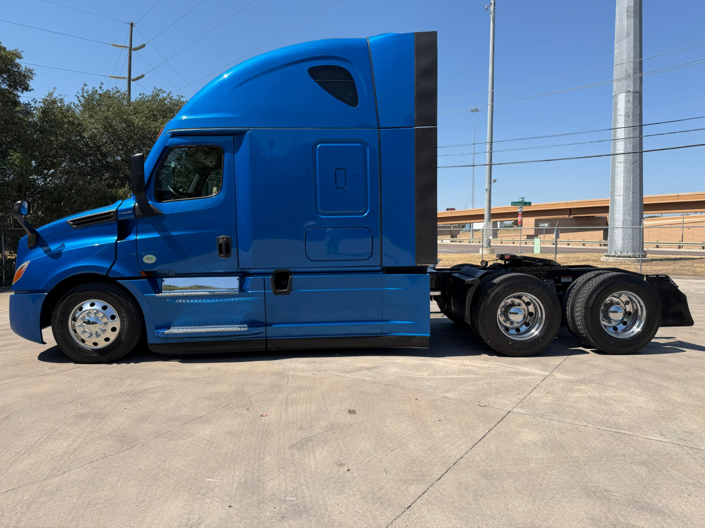 Truck cab side view showing blue Freightliner PT126064ST with sleeper, chrome steps, and dual rear axles.