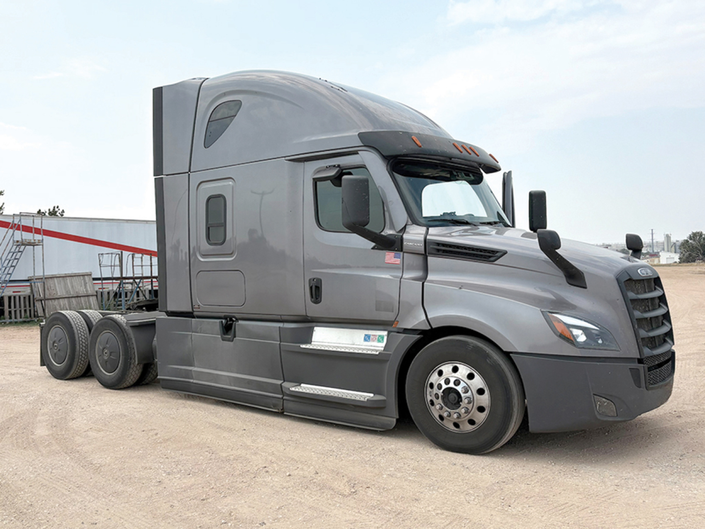 Truck cab exterior showing Freightliner Cascadia126 sleeper with gray paint, side mirrors, and wheel, advertisement plate area not visible.