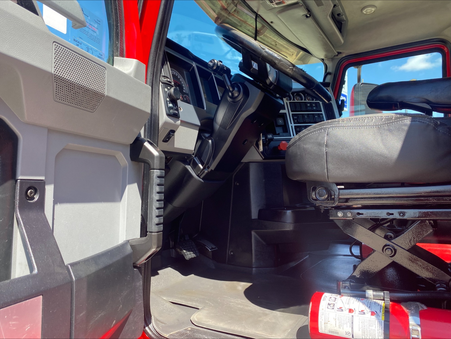 Truck cabin interior of a 2021 Mack ANTHEM, driver seat and dashboard visible, steering wheel, pedals, and door frame in view