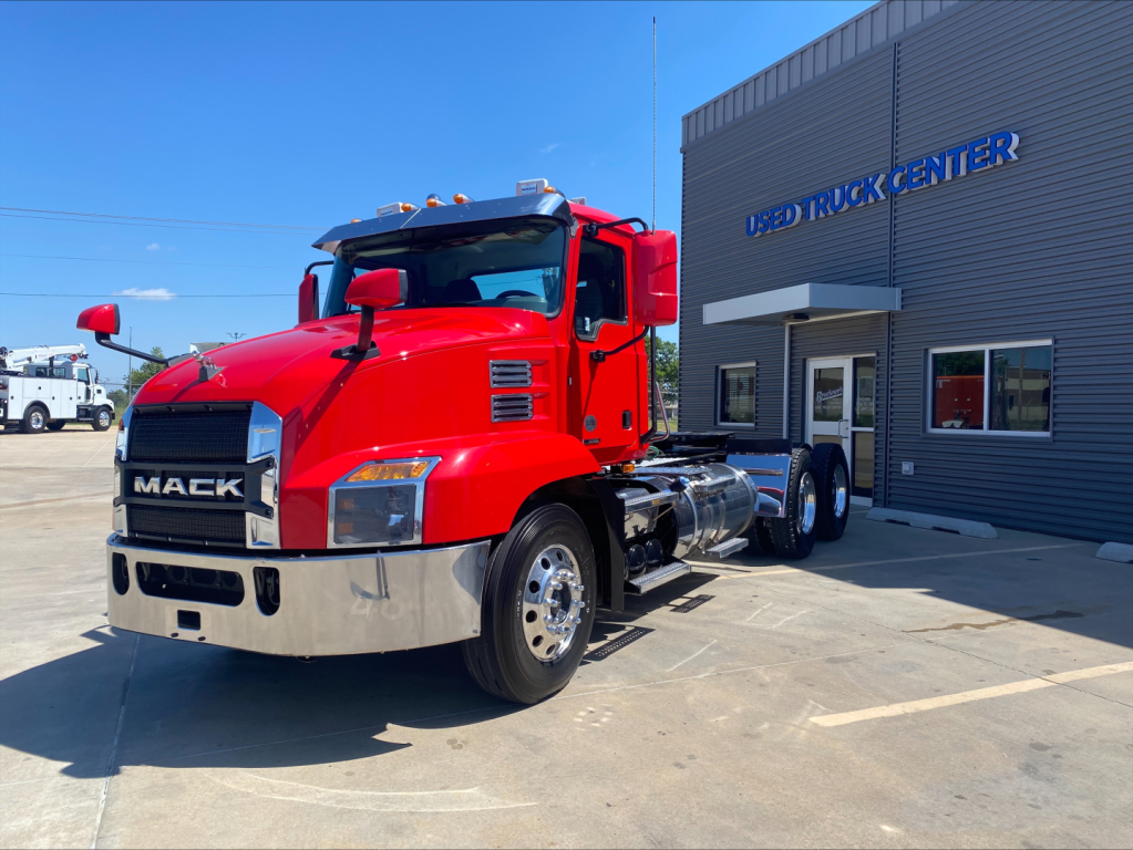 Mack Anthem truck in red cab parked outside Used Truck Center building with chrome bumper and dual rear axles.