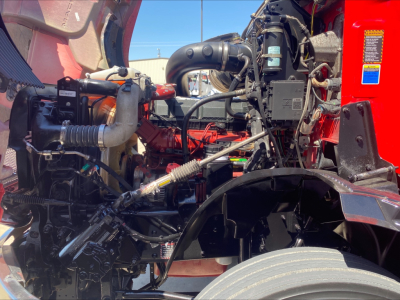 Engine bay of a 2021 Mack Anthem truck showing red engine block, hoses, wiring, and components in a daylight setting.