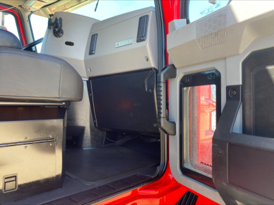 Truck cab interior of a 2021 Mack Anthem showing the driver side door open, dashboard panel, and storage area with beige/gray trim.