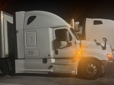 Truck cab side of a Freightliner Cascadia 2020 model 125 with DD13 engine, automatic transmission, white color, VIN plate visible, headlights on.