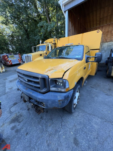 Ford F-550 Super Duty utility dump truck with yellow body and front bumper; cab shows some damage; dump bed behind; VIN plate not legible; other trucks in background.