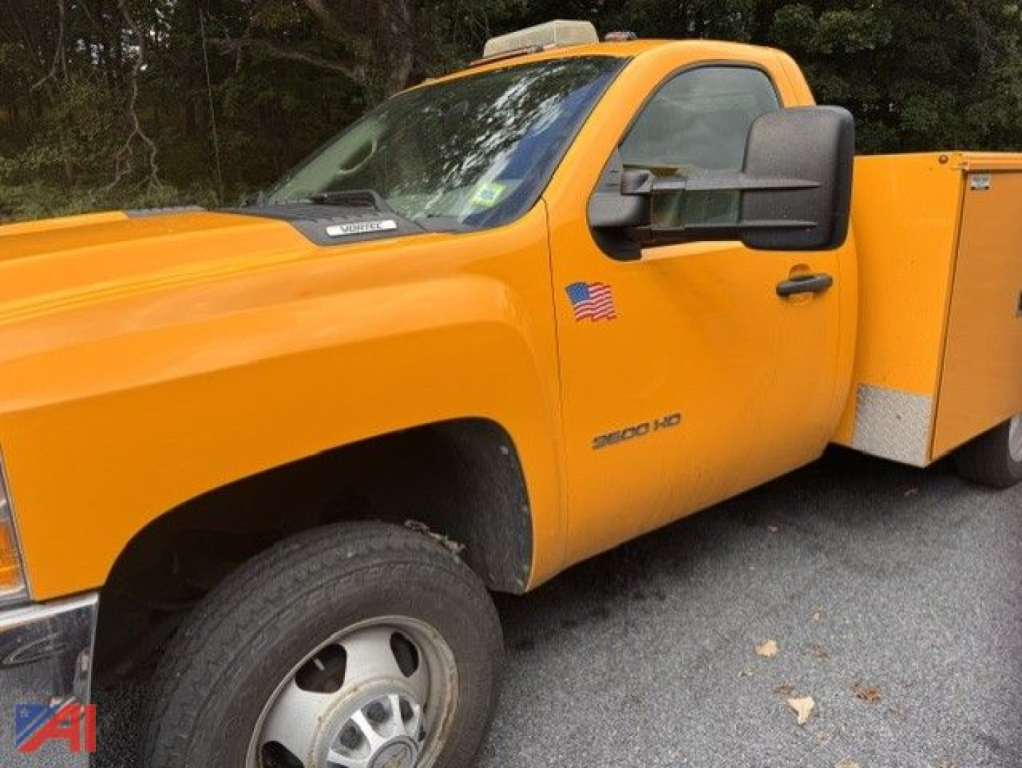 Chevrolet Silverado 3500HD utility truck side view showing orange cab and utility bed with chrome wheel and American flag decal.