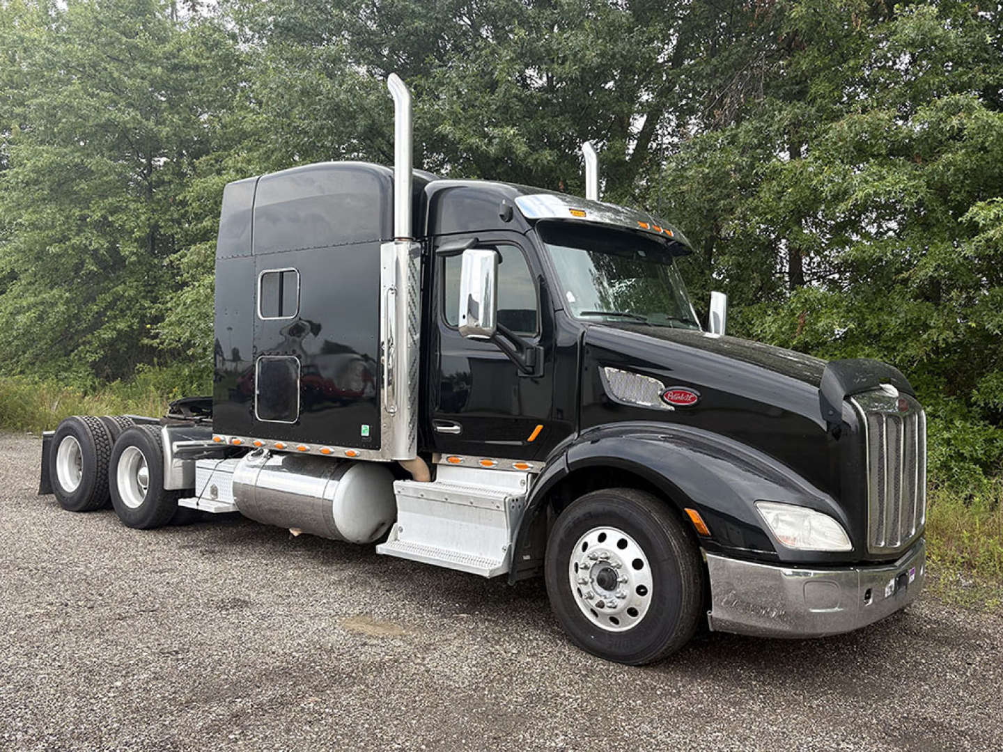 Peterbilt 579 UltraCab tractor in black, side view, with sleeper cab and chrome exhaust stacks, 3-axle configuration, diesel fuel tanks visible.